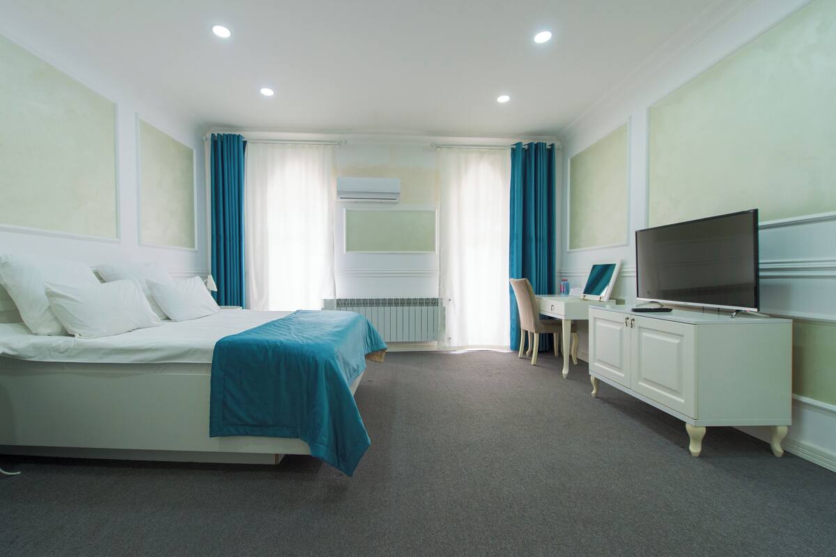 Una camera d'albergo con un letto, una scrivania, una televisione e un termosifone.