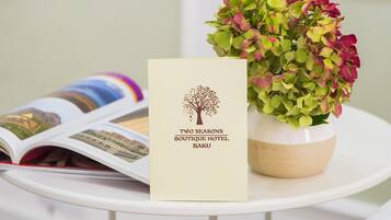 A brochure titled "Two Seasons Boutique Hotel Baku" and a potted plant with green and red leaves on a white table.