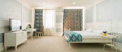 A hotel room with a bed, a desk, a chair, a TV, and a bedside table with a phone and a vase.