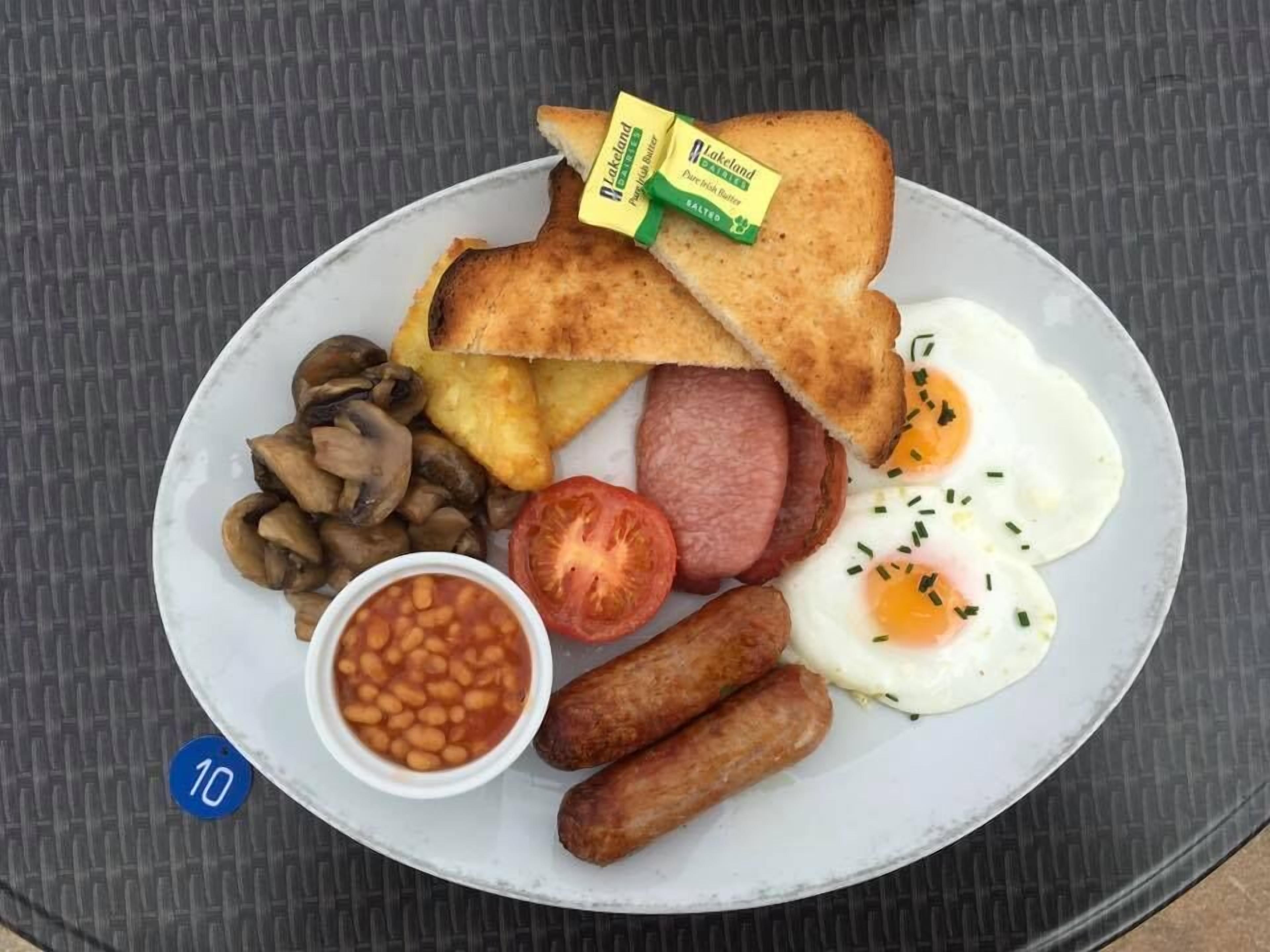 Une assiette de nourriture pour le petit-déjeuner comprenant des toasts, des œufs, des saucisses, des champignons, des haricots et une tomate.