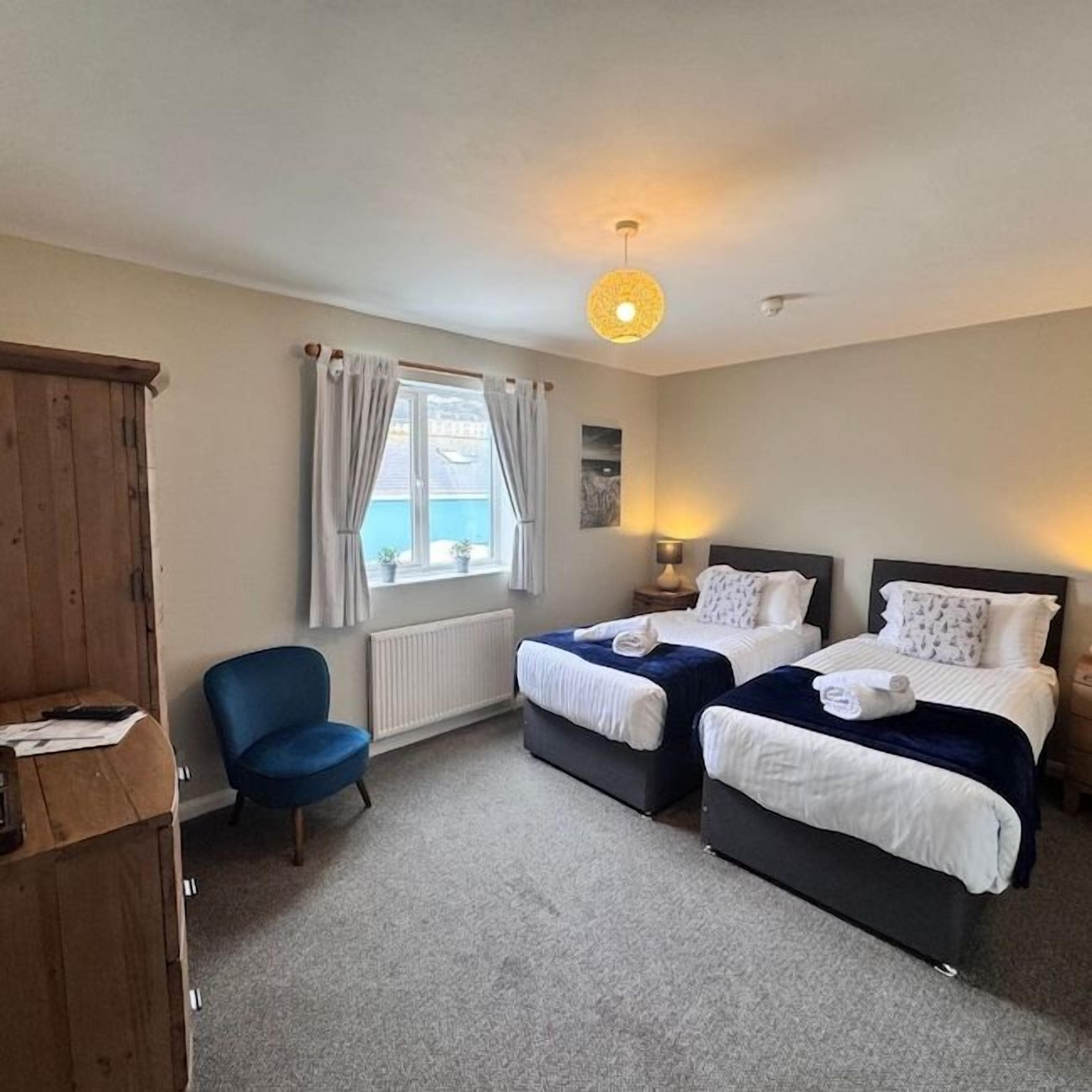 A room with two beds, a chair, a wooden cabinet, and a window with curtains.