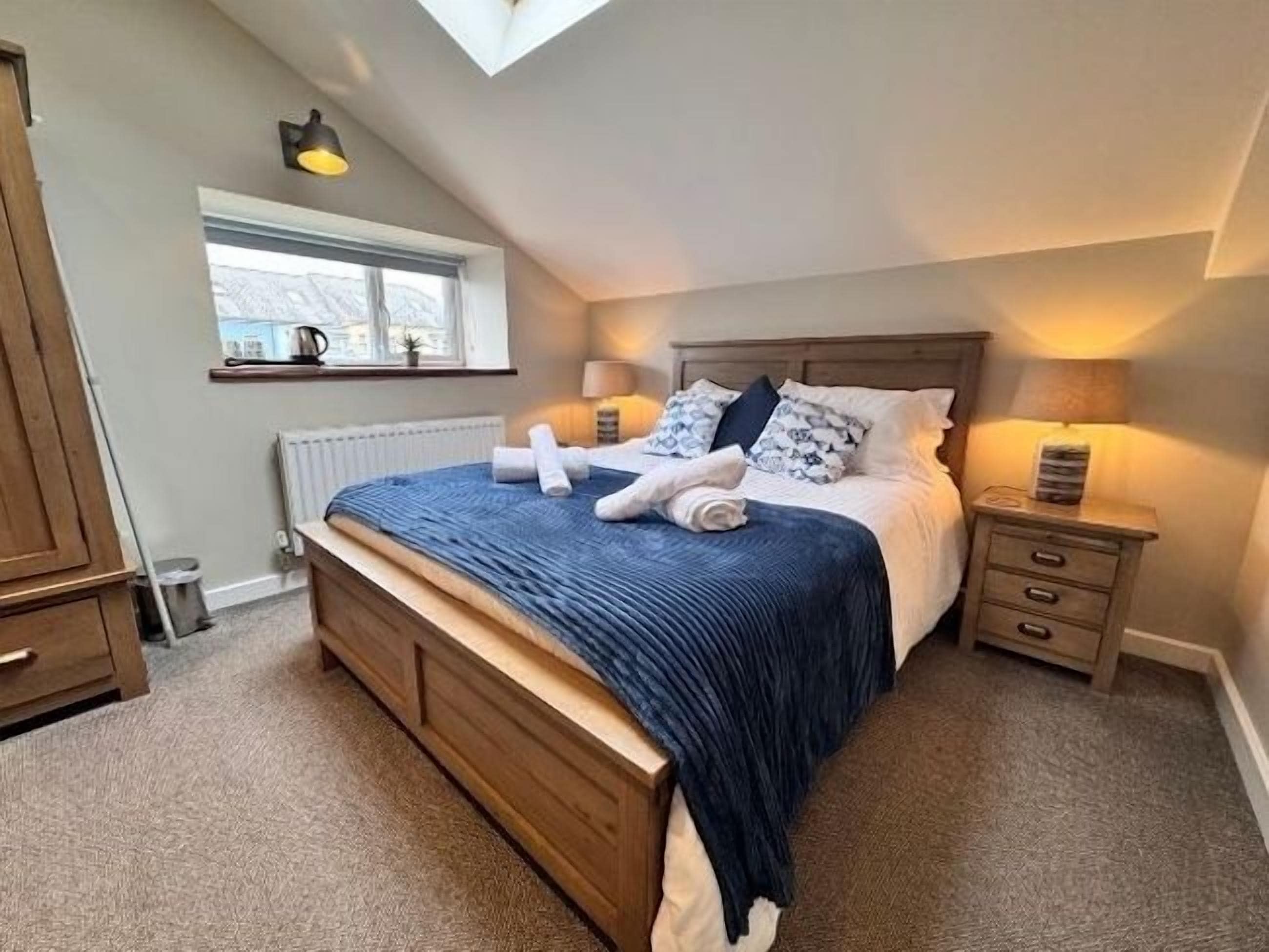 A bedroom with a large bed, bedside tables, a window, and a skylight.