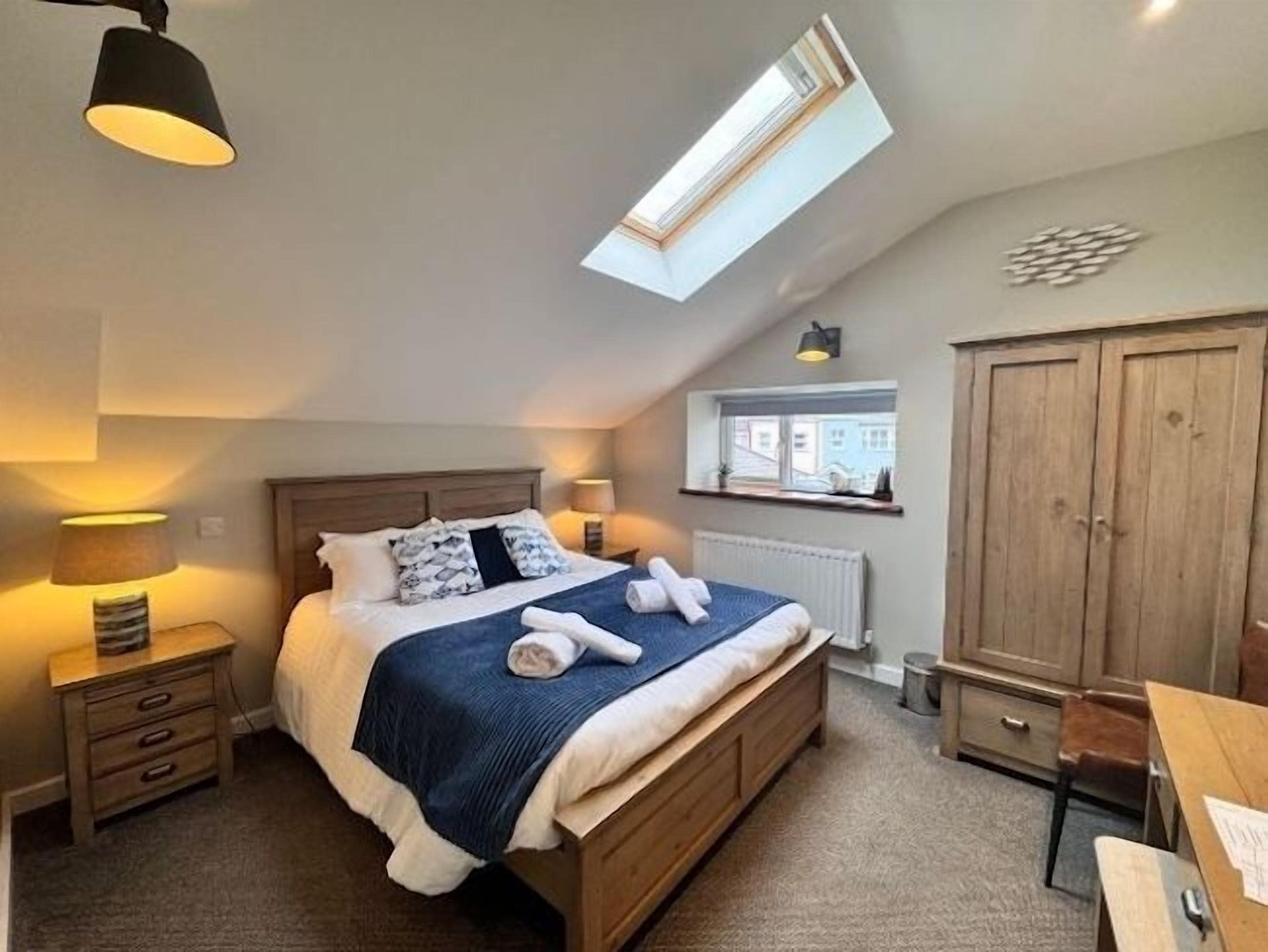 A bedroom with a bed, bedside tables, a window, a wardrobe, and a skylight.
