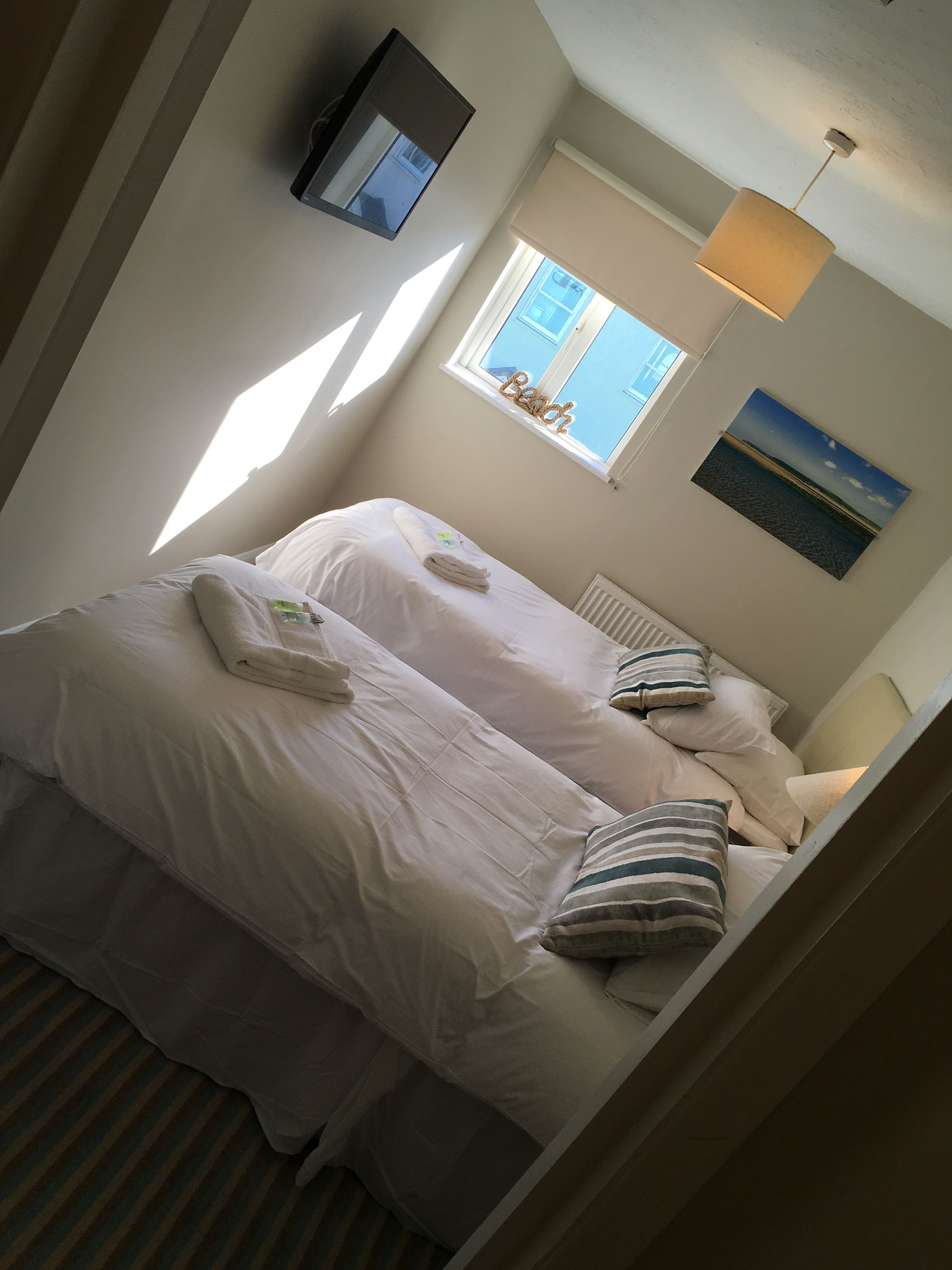 A bedroom with two beds, a window with a view of buildings, a wall-mounted lamp, and a painting.