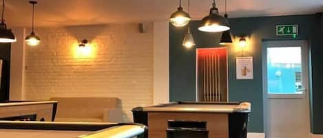 A pool table in a room with a brick wall, multiple hanging lights, and a door with an exit sign.