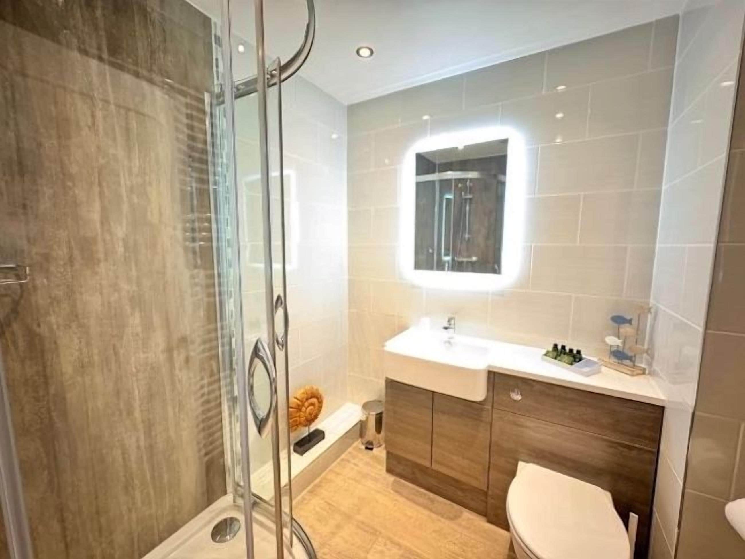 Un baño moderno con cabina de ducha de vidrio, tocador con espejo y inodoro.