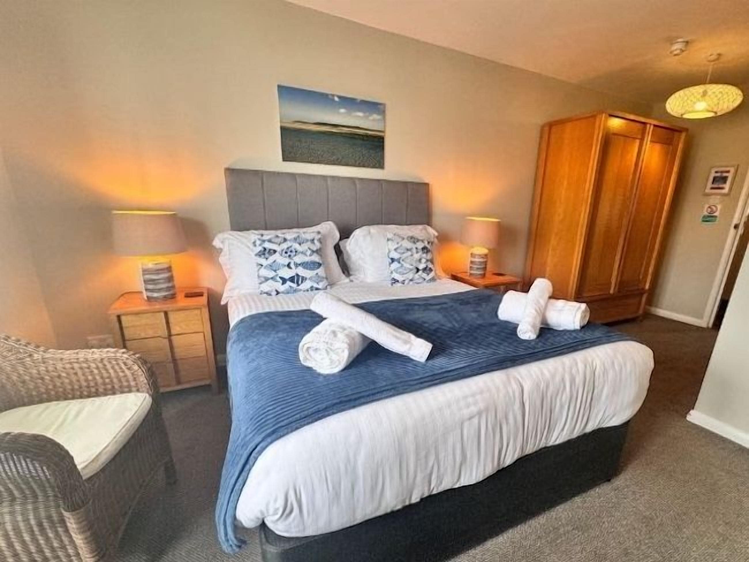 A hotel room with a bed, a nightstand, a lamp, a wardrobe, and a chair.