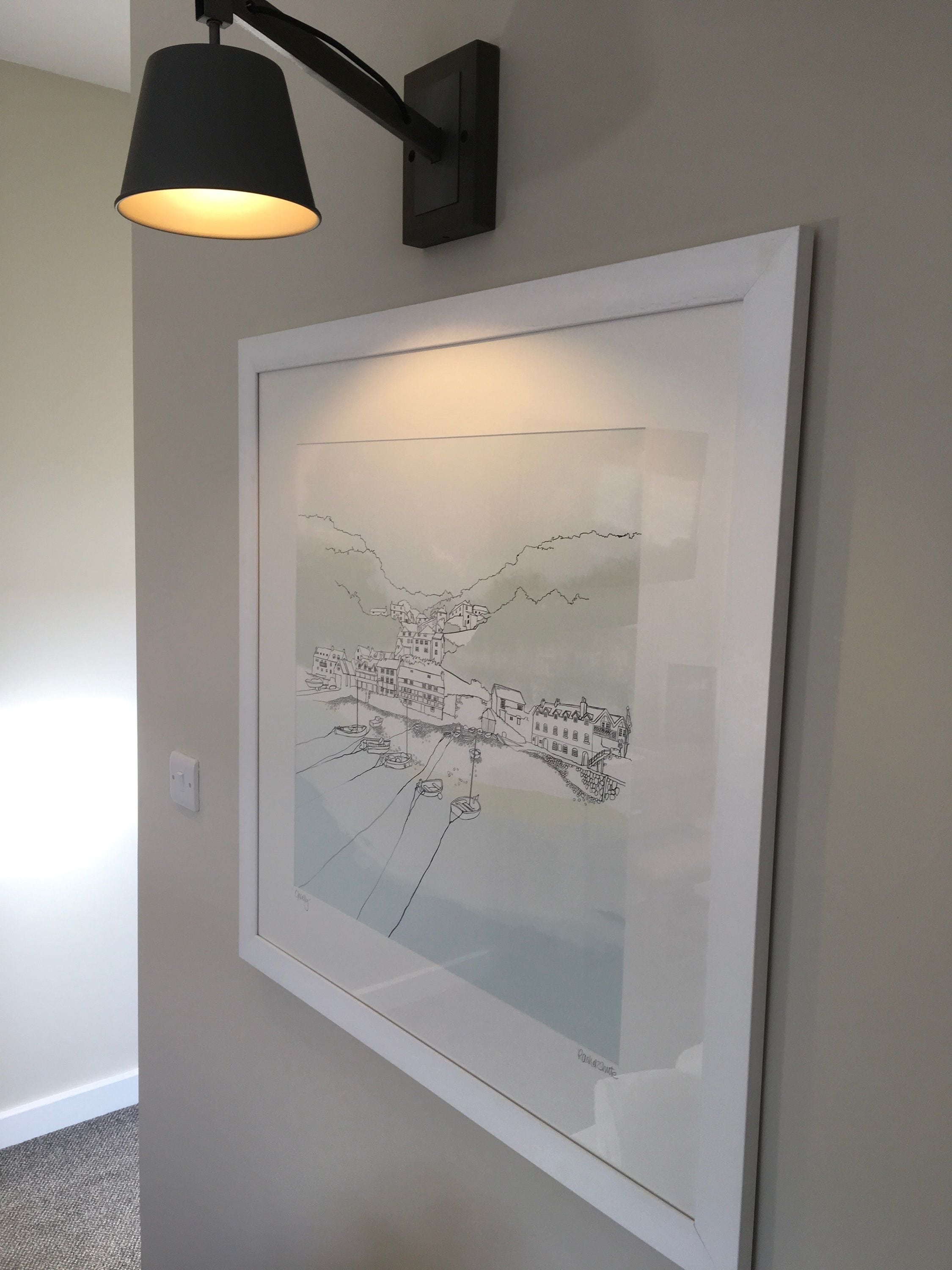 A framed black and white cityscape artwork on a wall, a black wall-mounted lamp, and a white switch.