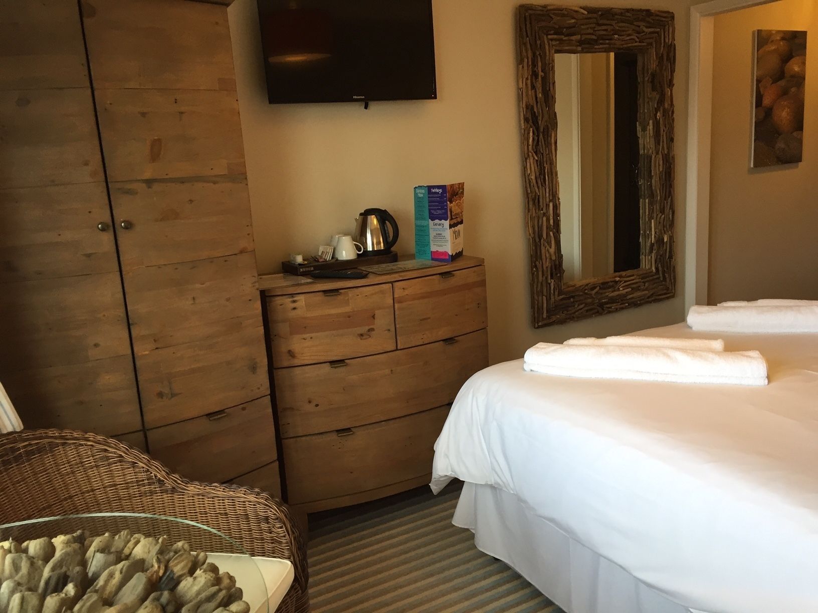 A hotel room with a wooden wardrobe, a television, a mirror, a bed with white linens, and a wicker chair.