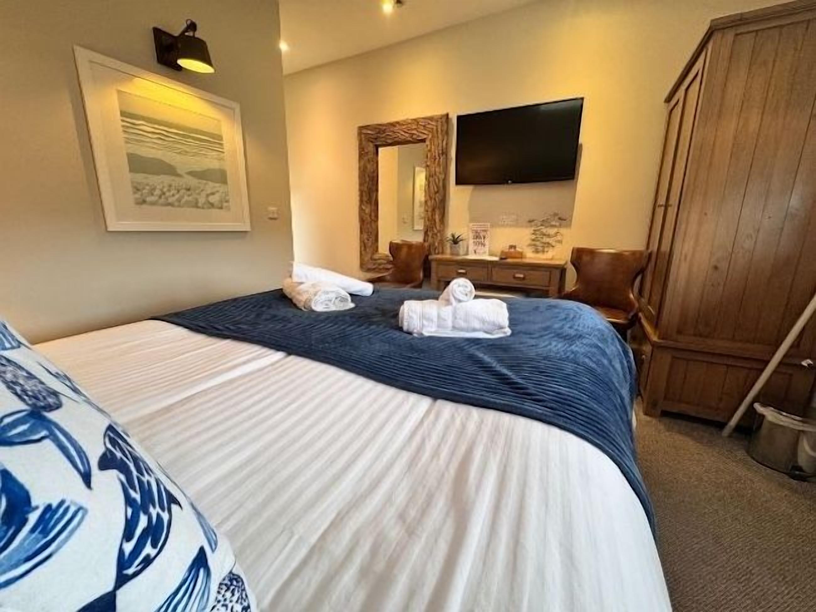 A hotel room with a bed, a television, a wardrobe, and a painting on the wall.