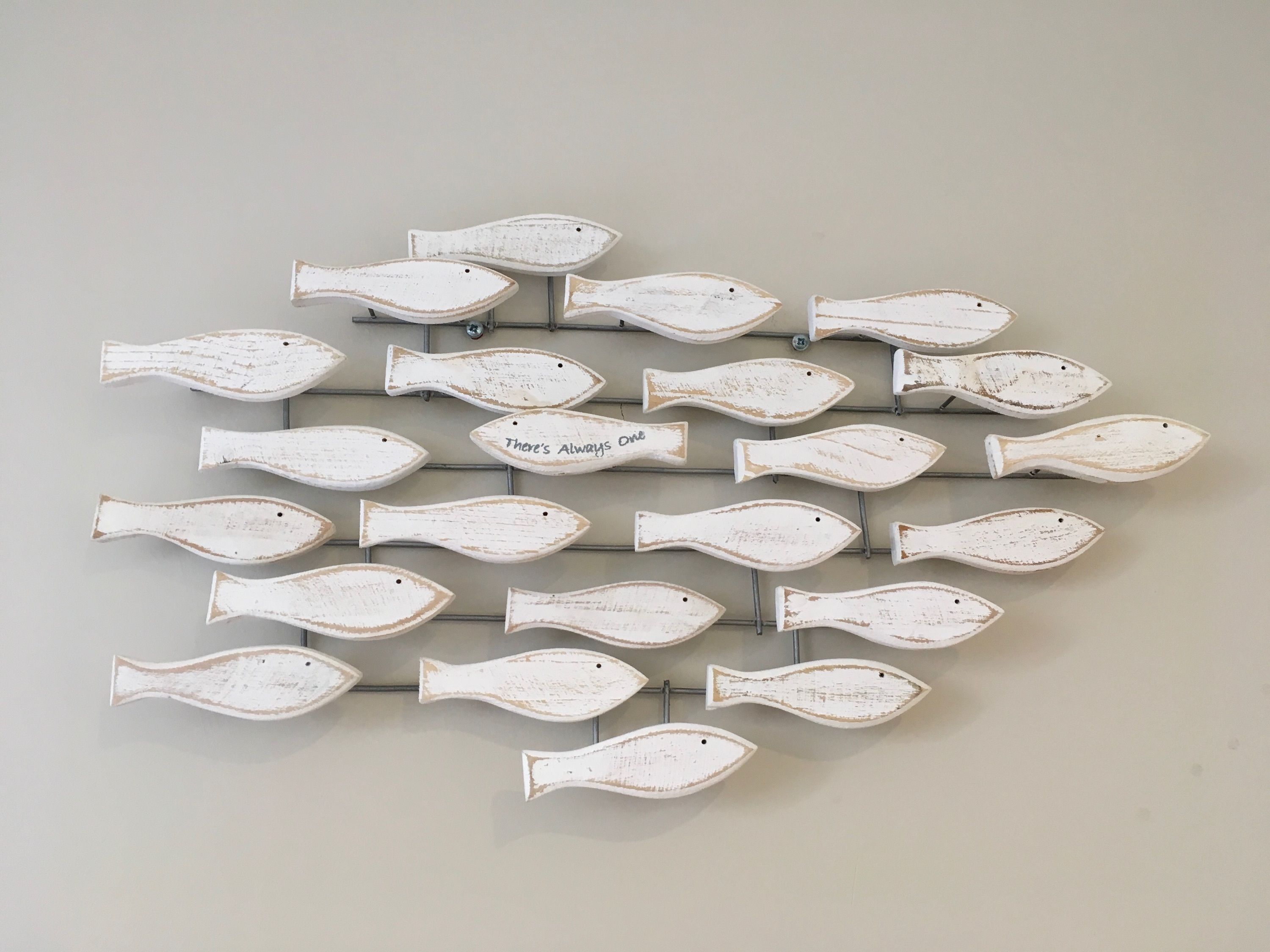 Una pared decorada con varias figuras blancas con forma de pez, algunas con texto.