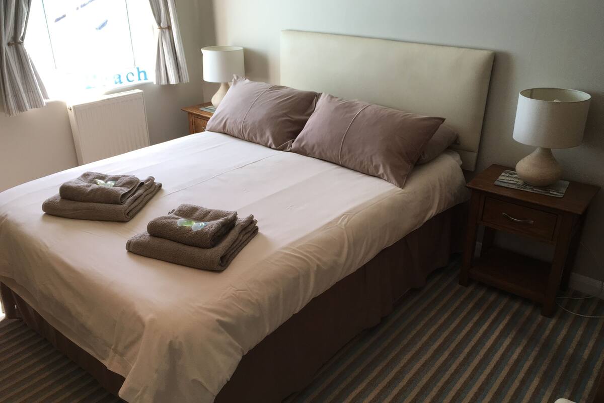 Cama bem arrumada com toalhas dobradas, cabeceira, duas mesas de cabeceira com abajures e um tapete listrado.