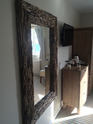 A room with a large woven mirror, a wooden cabinet with decorative items, and a television mounted on the wall. - The Waterfront Inn (Bideford)