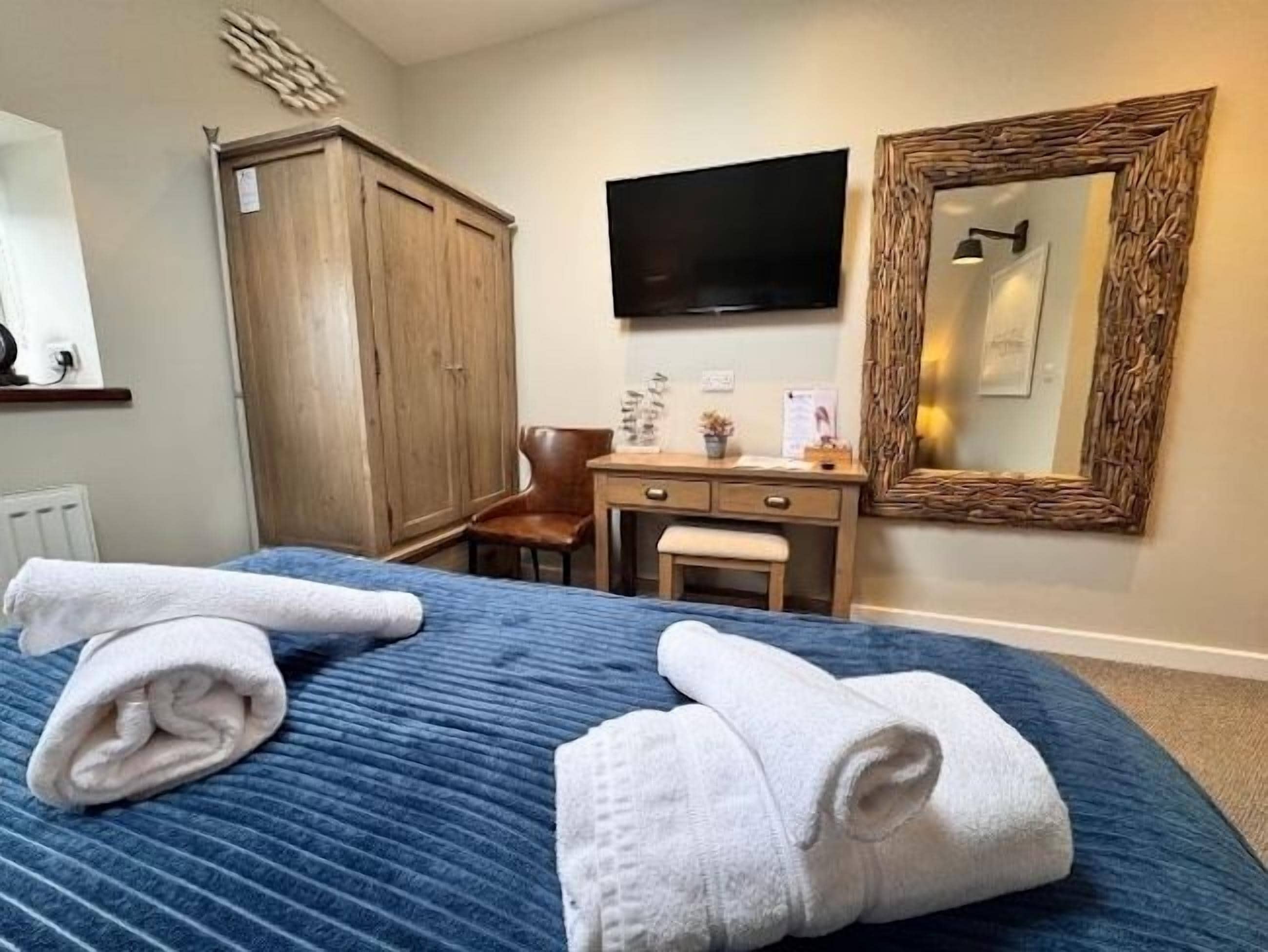 A hotel room with a bed, a desk, a chair, a wardrobe, a television, and a mirror.