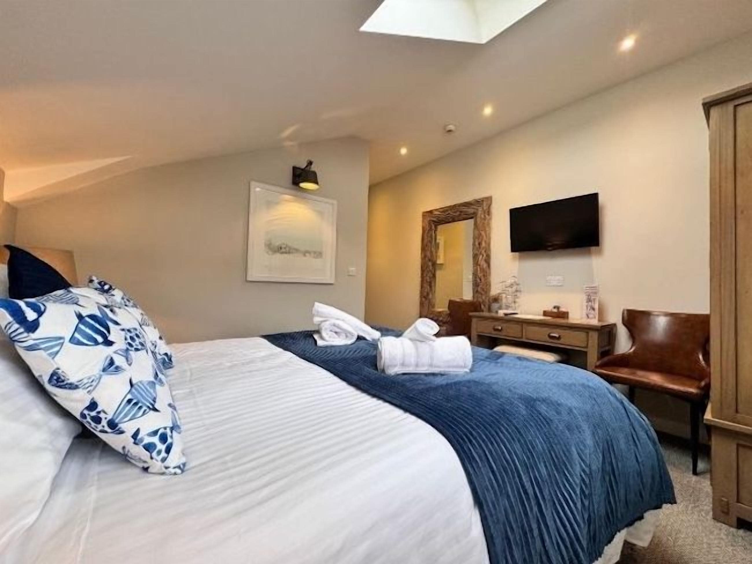 Habitación de hotel con una cama, un escritorio, una silla, un televisor y un espejo.
