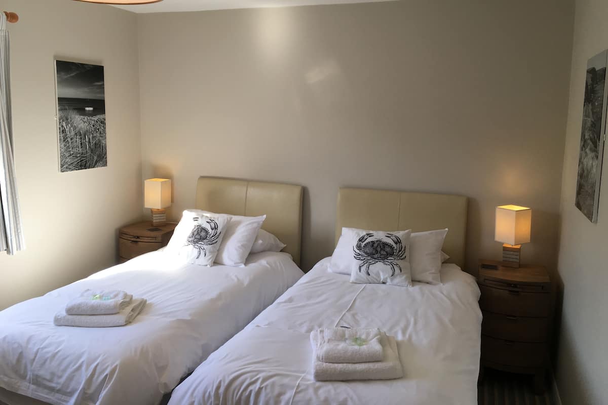Quarto de hotel com duas camas, cada uma com cabeceira, abajures e toalhas.