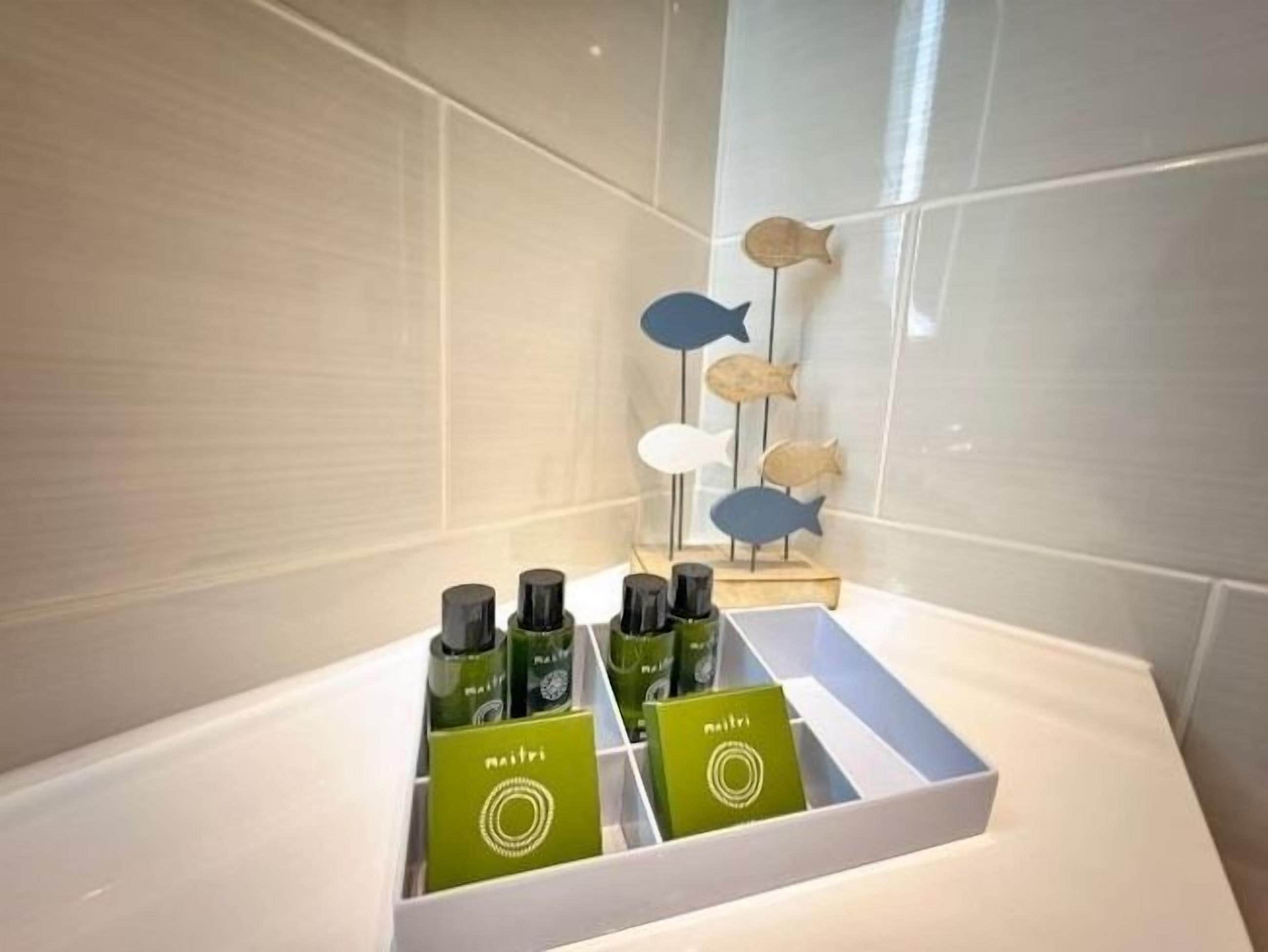 Un baño con un lavamanos blanco, un espejo y una repisa con botellas y una decoración de peces.