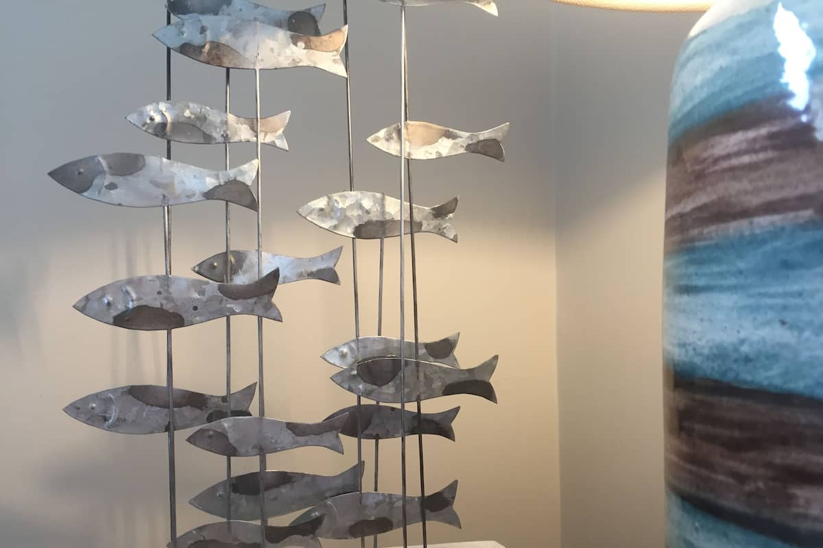 Escultura de metal representando peixes sobre um pedestal branco.