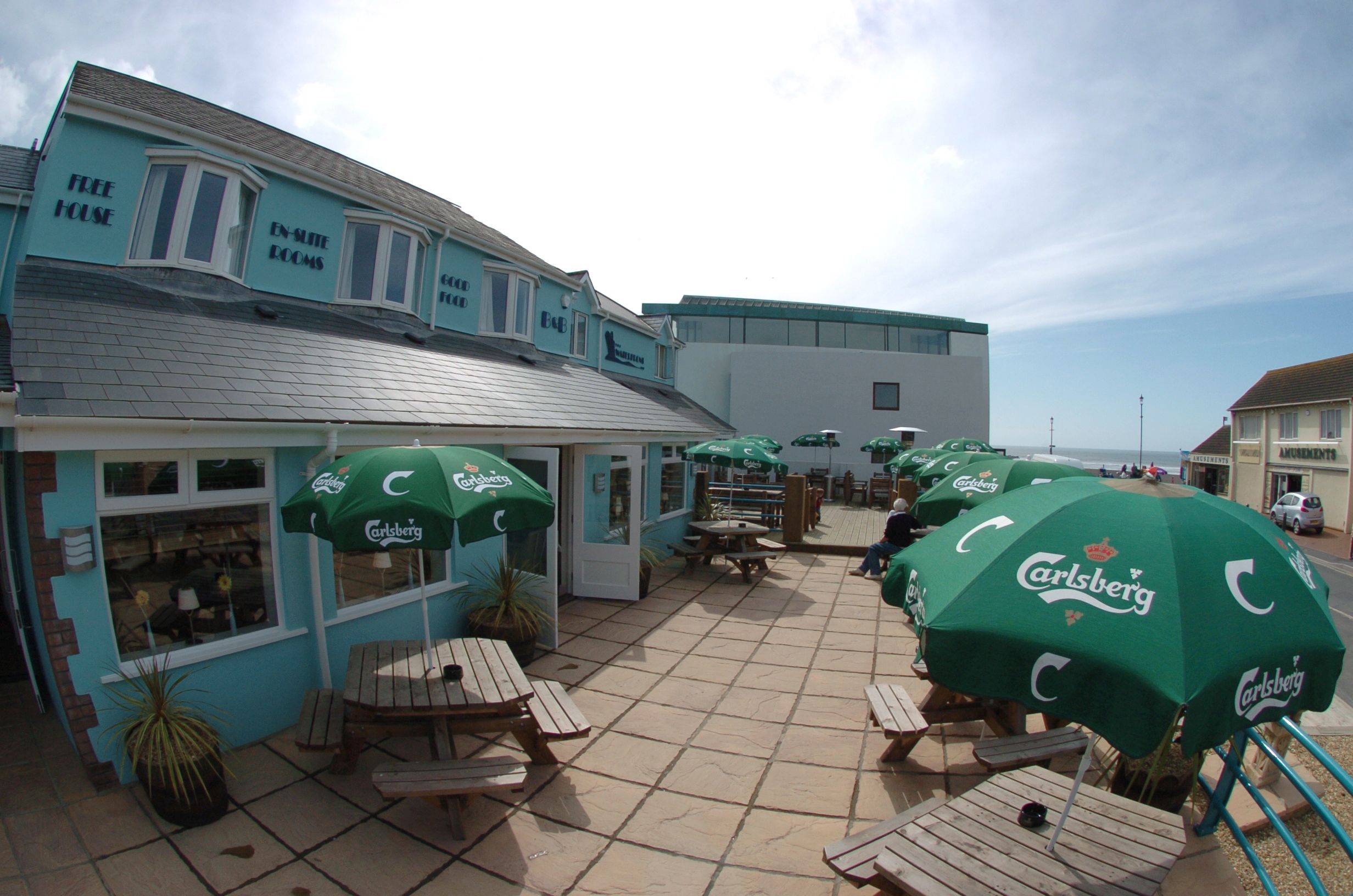 A seaside hotel with outdoor seating and Carlsberg branded umbrellas.