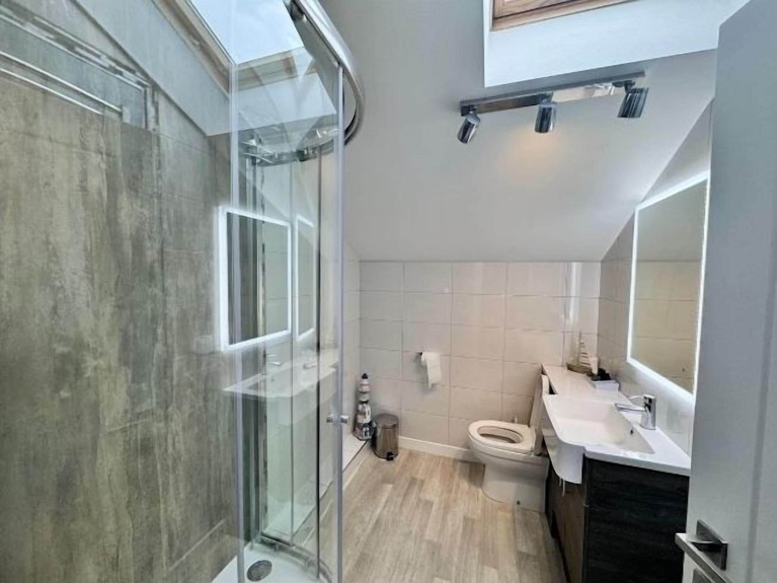 Un baño moderno con cabina de ducha de vidrio, inodoro y lavamanos con espejo.