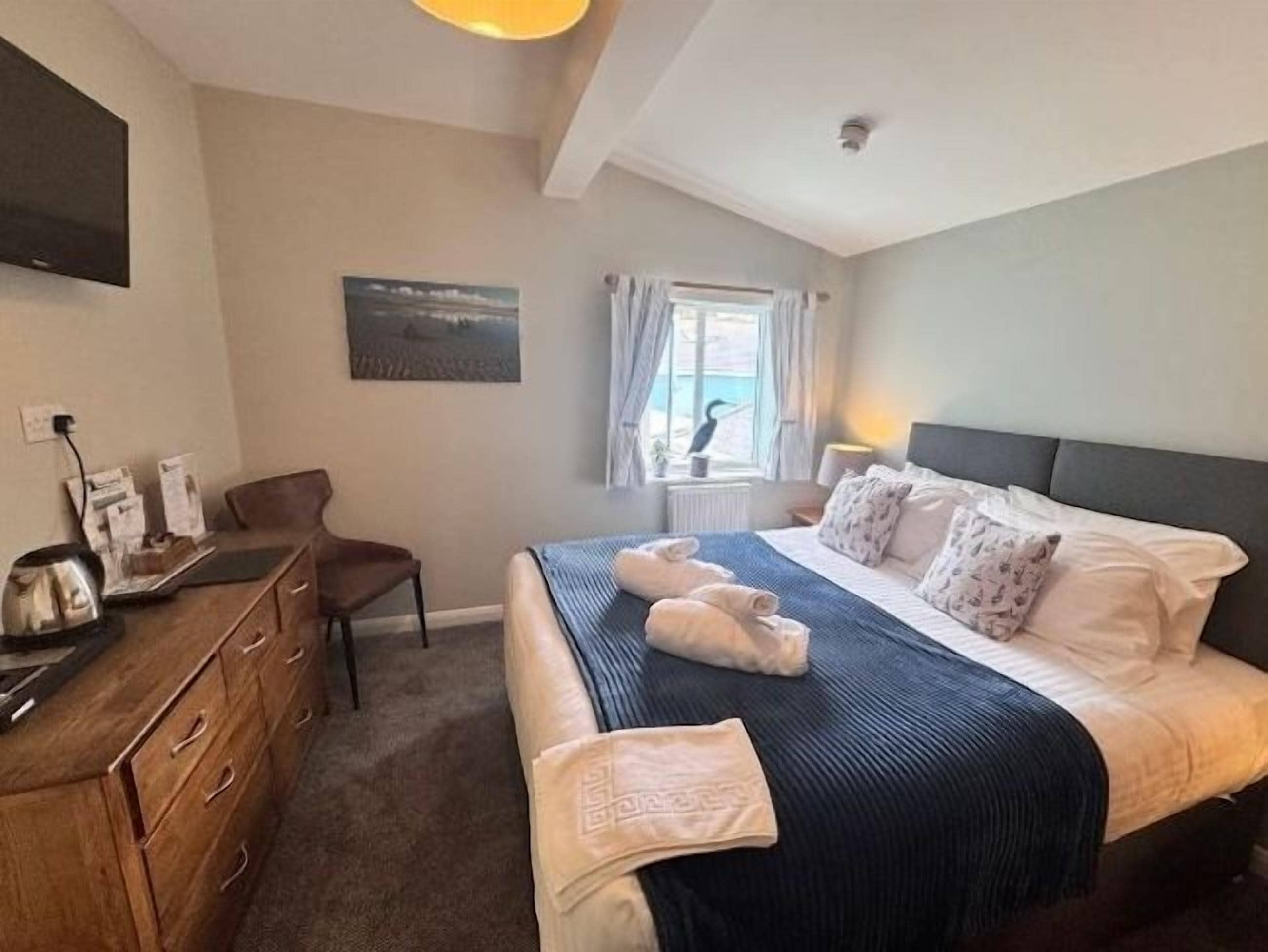 A bedroom with a bed, a desk, a chair, and a window with curtains.