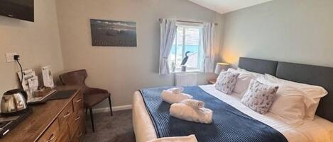 A bedroom with a bed, a desk, a chair, and a window with curtains.