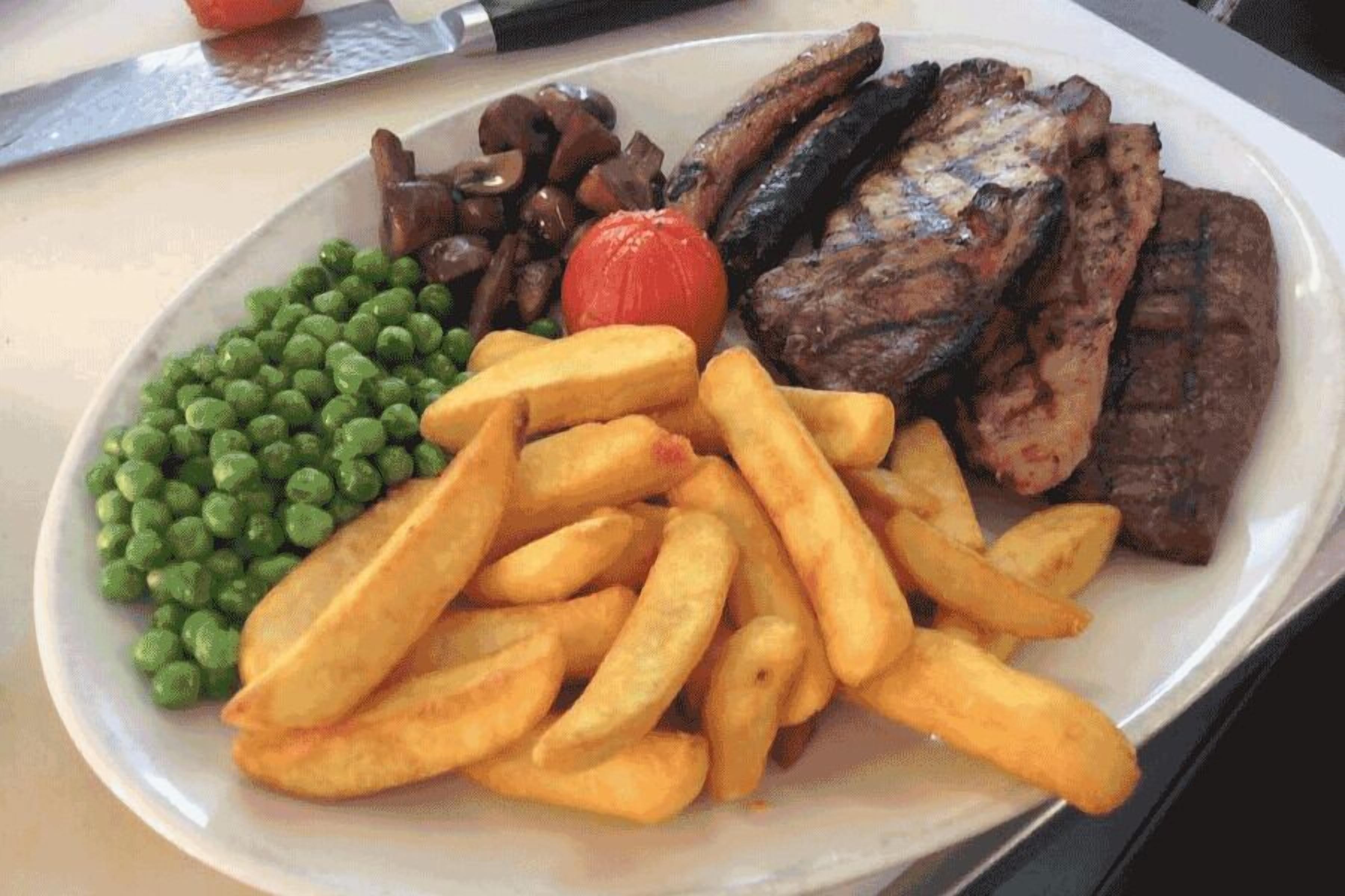 A plate with grilled meat, mushrooms, peas, and fries.