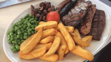 A plate with grilled meat, mushrooms, peas, and fries.