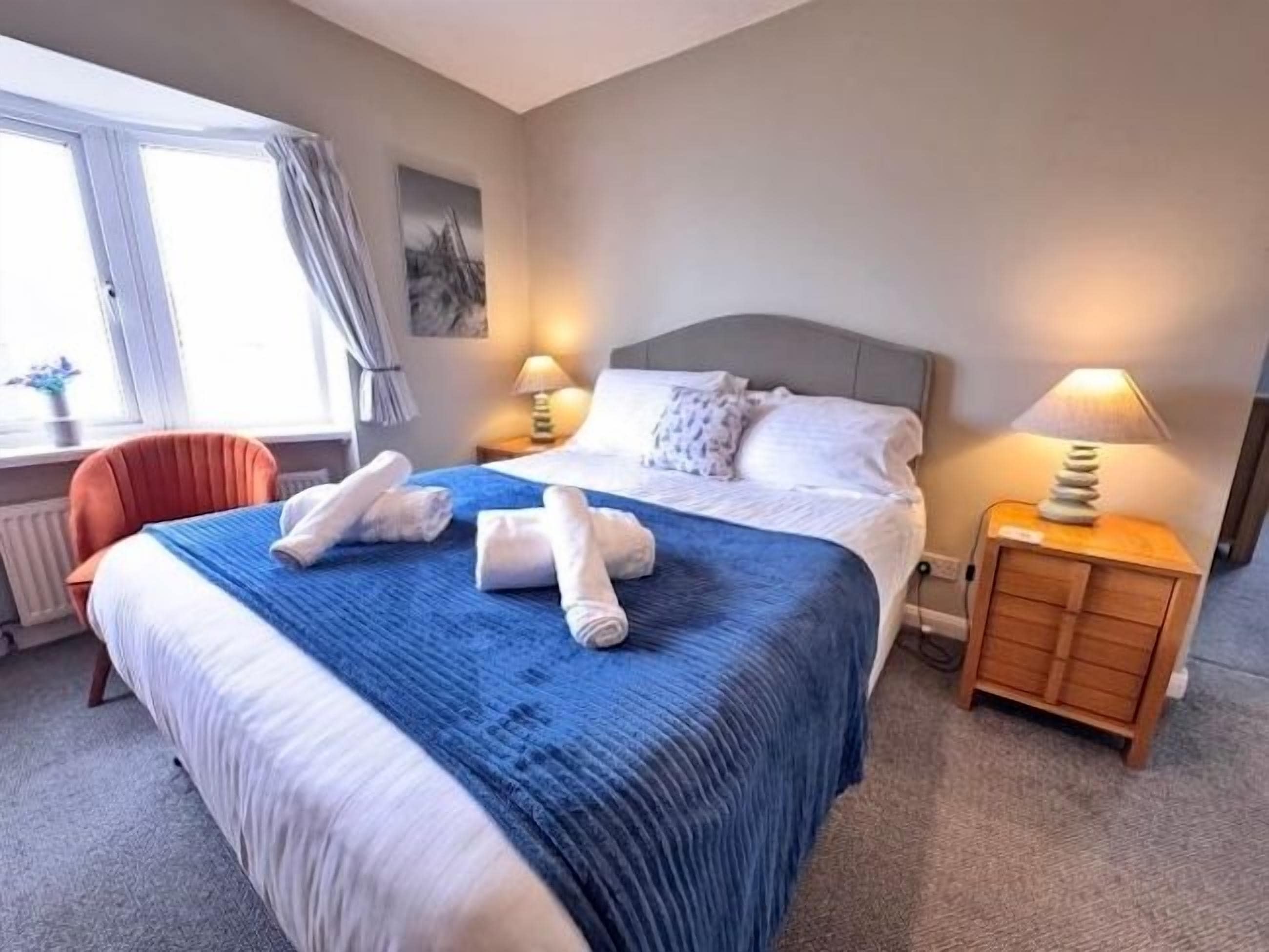 A hotel room with a bed, two bedside lamps, a chair, and a window with curtains.