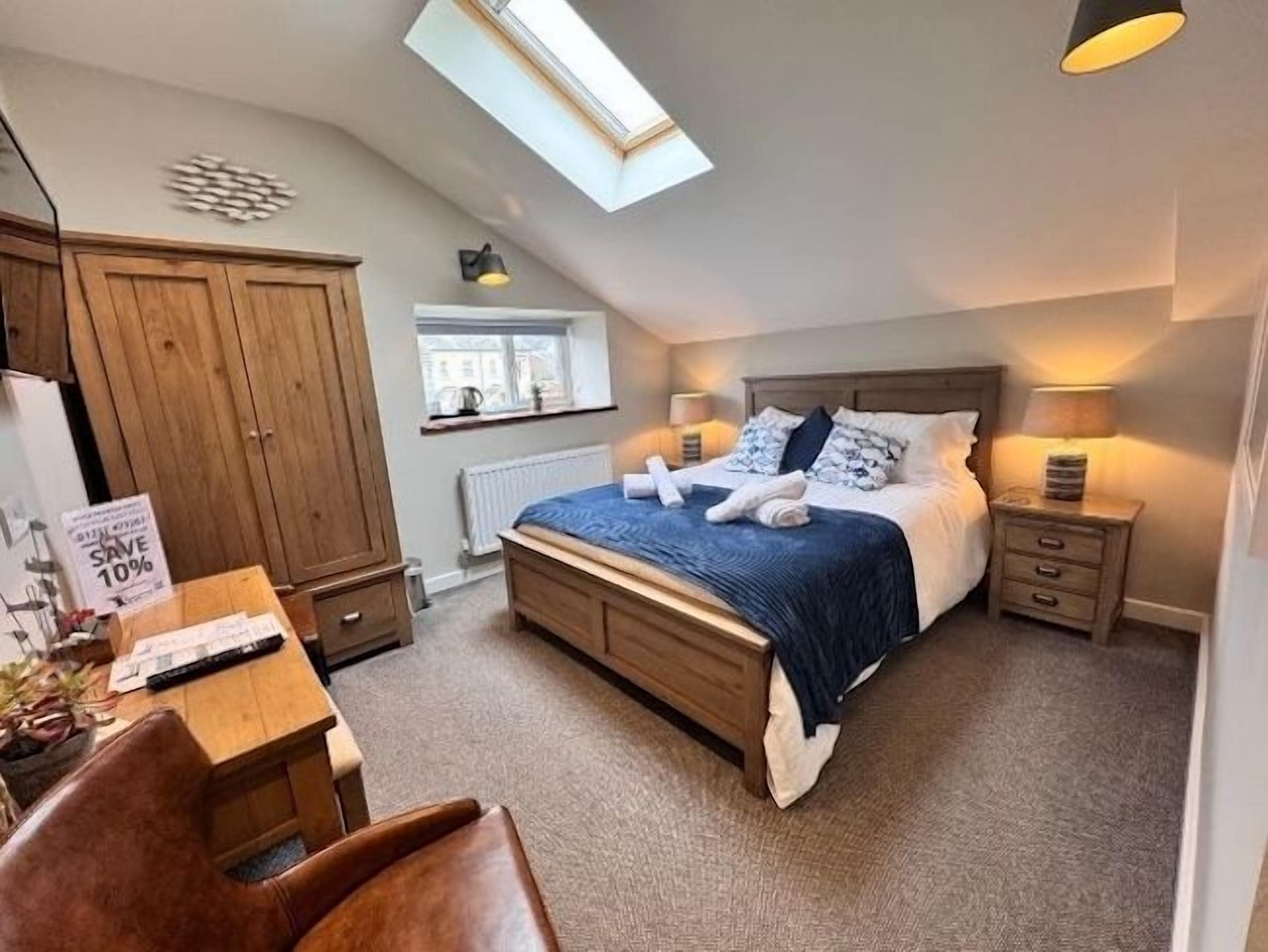 A bedroom with a bed, bedside tables, a desk, a chair, a wardrobe, a skylight, and a window.