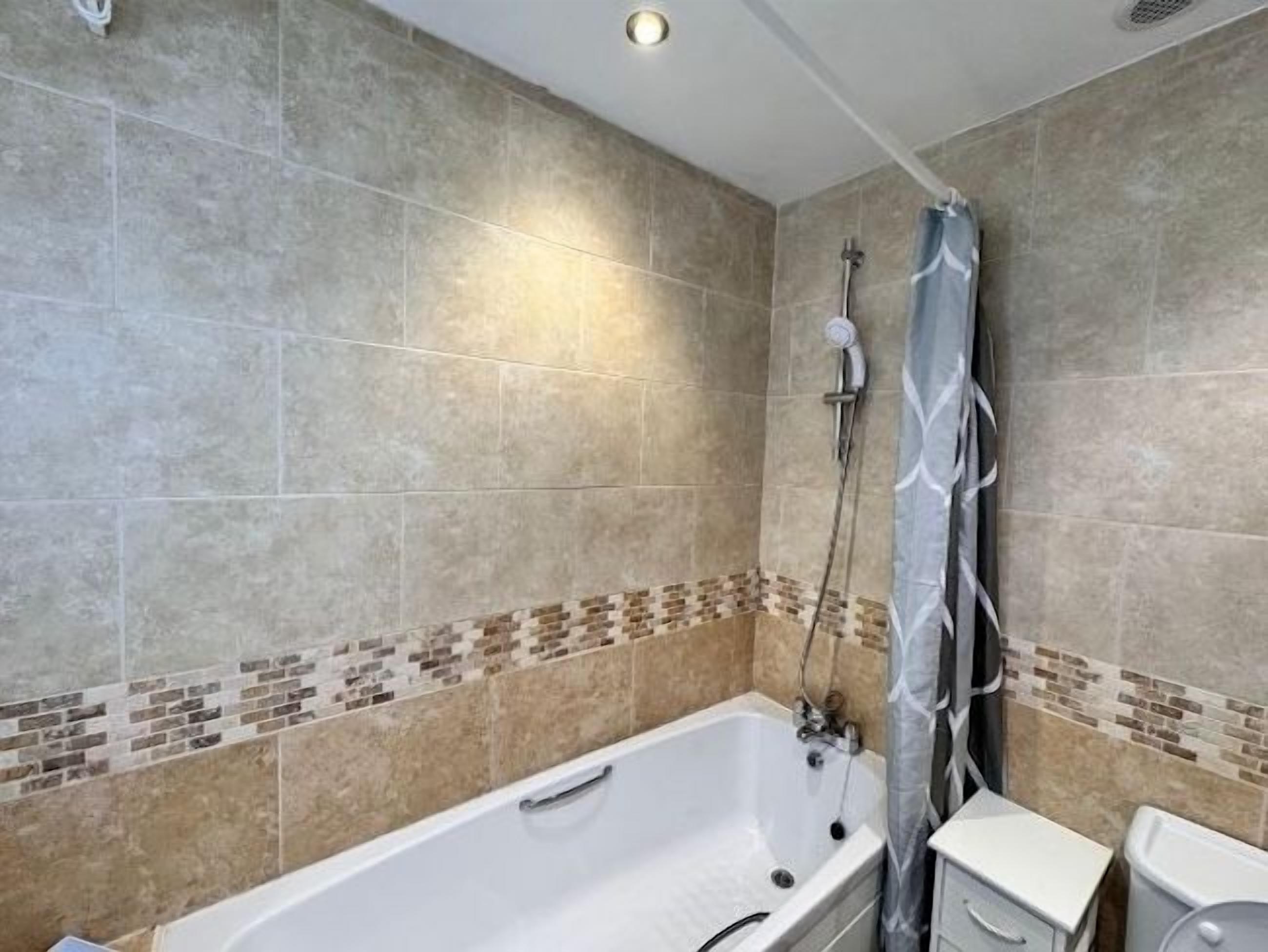 Een badkamer met een bad, douche en betegelde wanden.