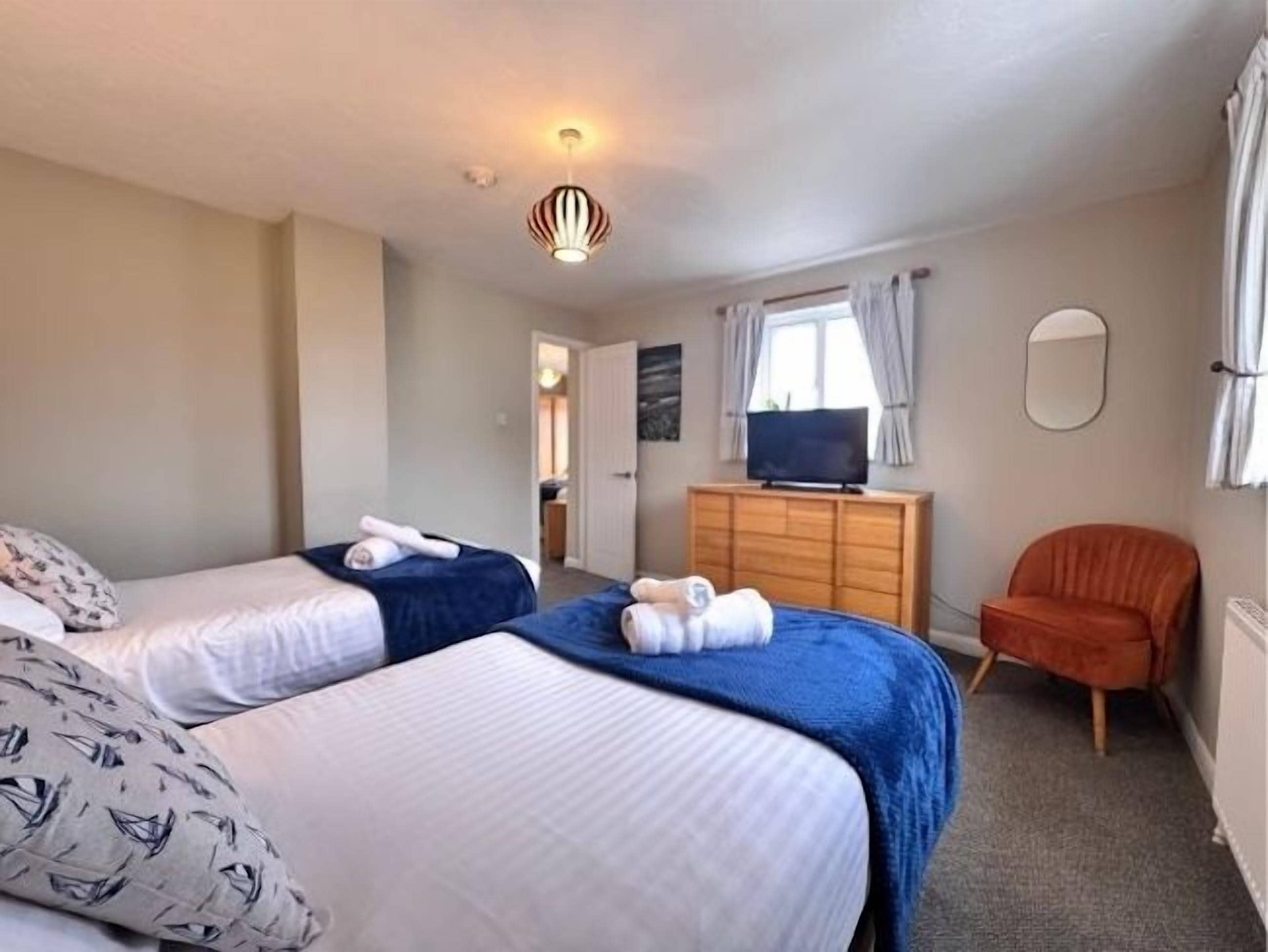 A hotel room with two beds, a wooden dresser, a television, and a chair.