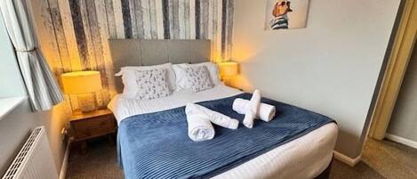 Una habitación de hotel con una cama grande, un cabecero con estampado a rayas, una mesita de noche con lámpara y un cuadro enmarcado en la pared.