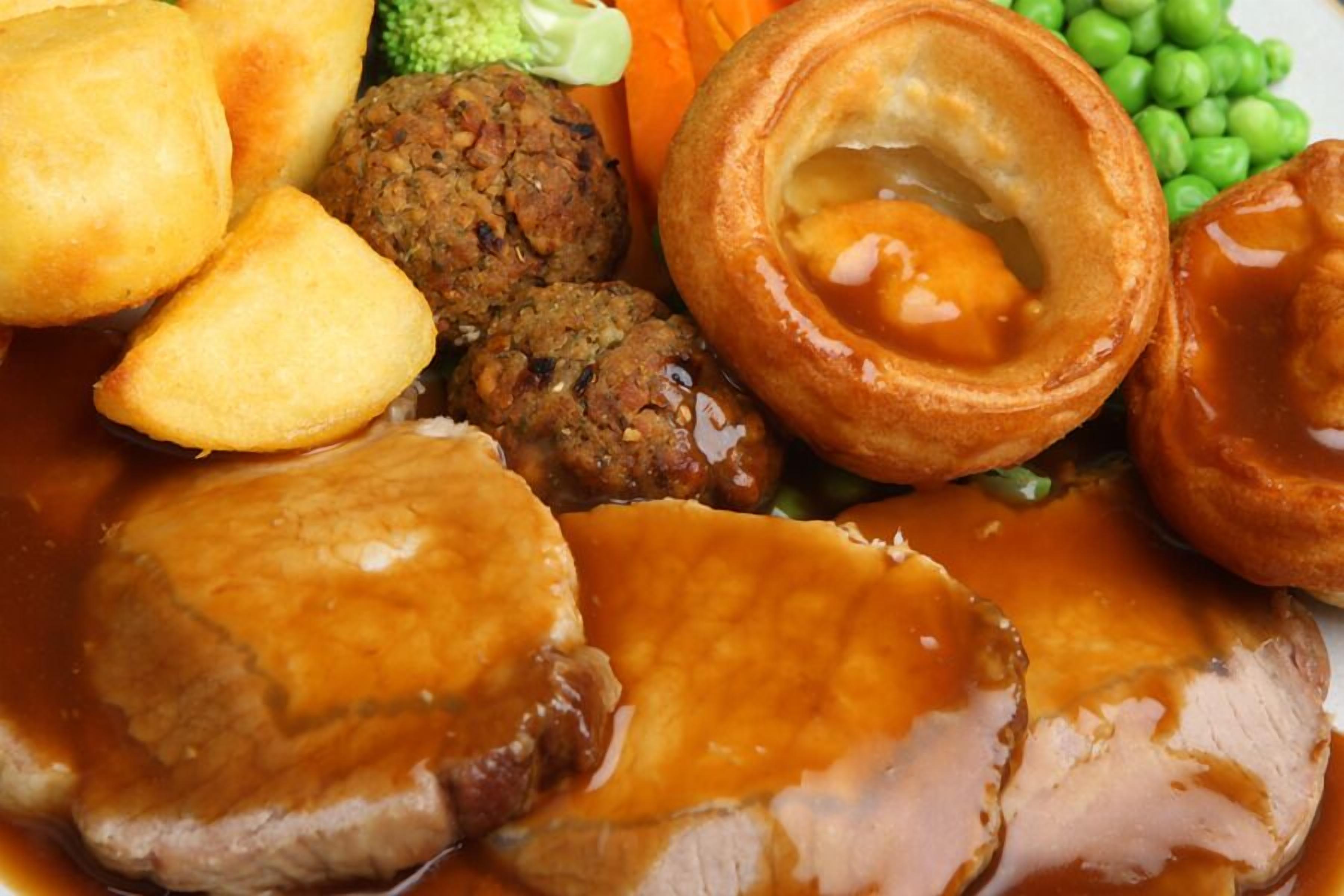 A plate of food including roast beef, Yorkshire pudding, Yorkshire pudding with egg, and vegetables.