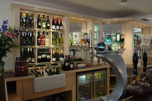Zona de bar con estantes de bebidas embotelladas, sistema de grifos y un refrigerador.
