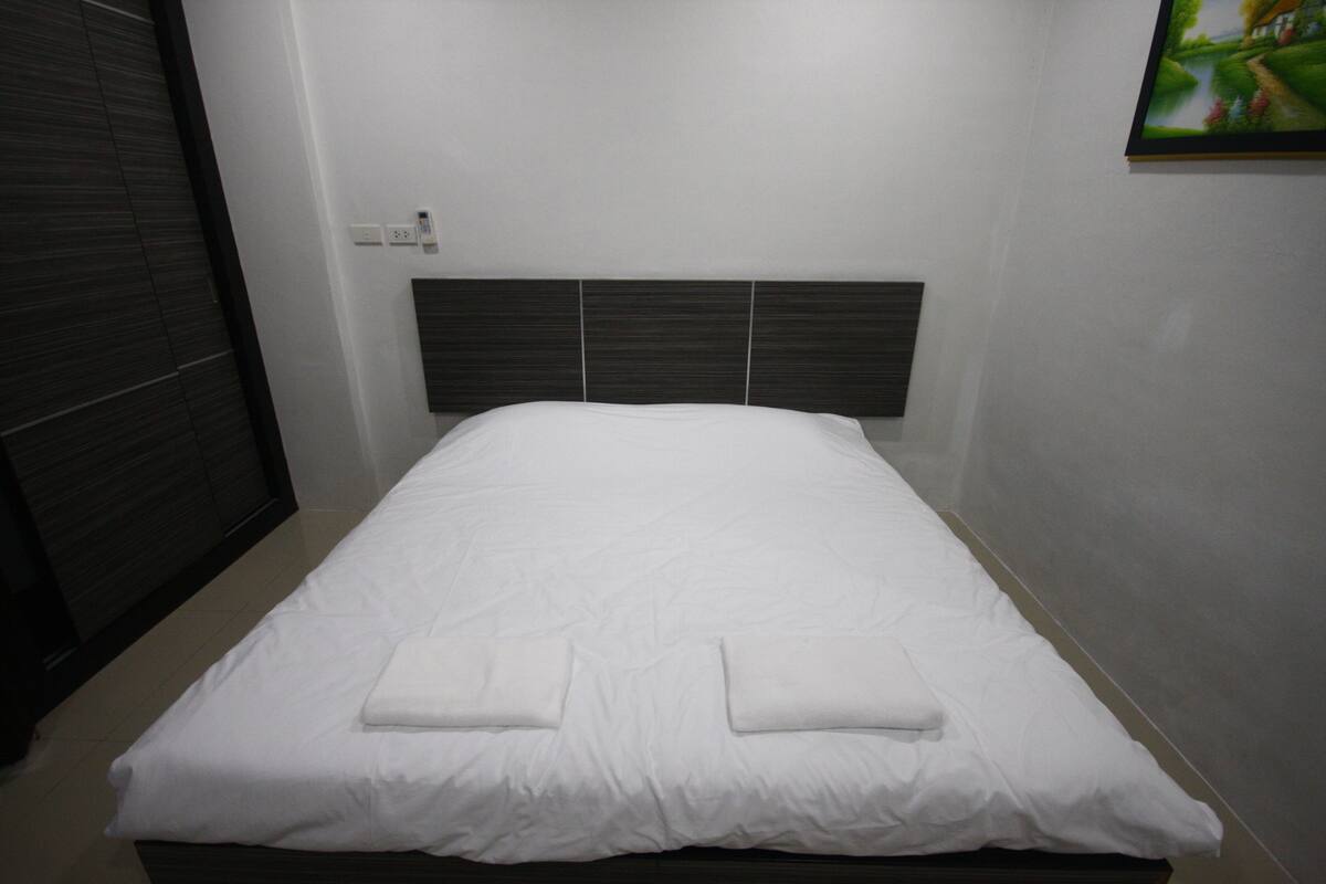 A neatly made bed with white linens and two folded towels on the bed.