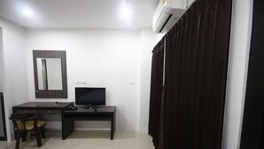 A hotel room with a desk, chair, television, and an air conditioning unit. - Suchada Palace (Thung Song)