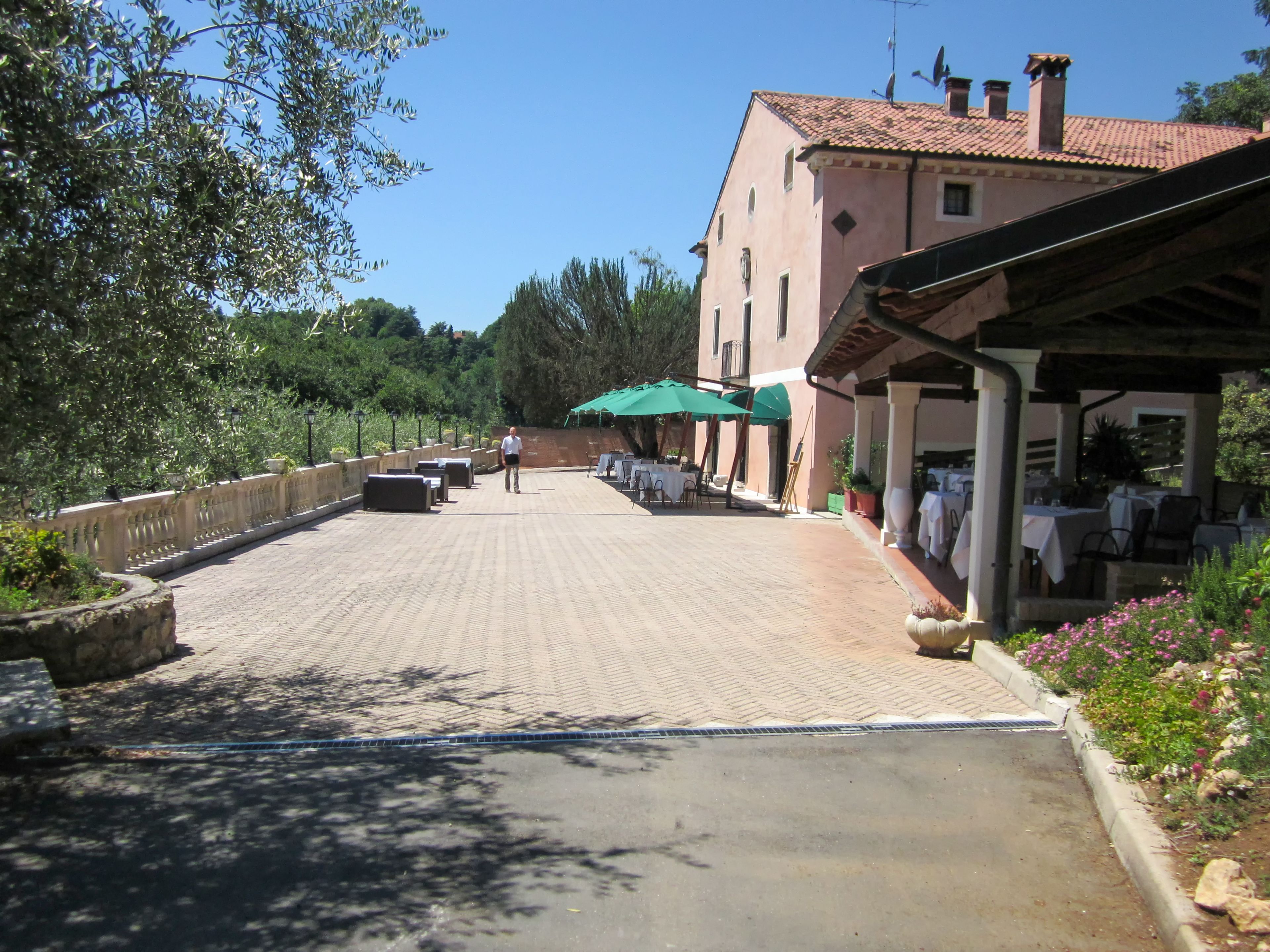 A paved courtyard with outdoor seating, a building with a tiled roof, and greenery.