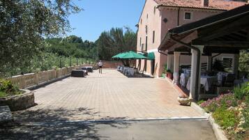A paved courtyard with outdoor seating, a building with a tiled roof, and greenery.