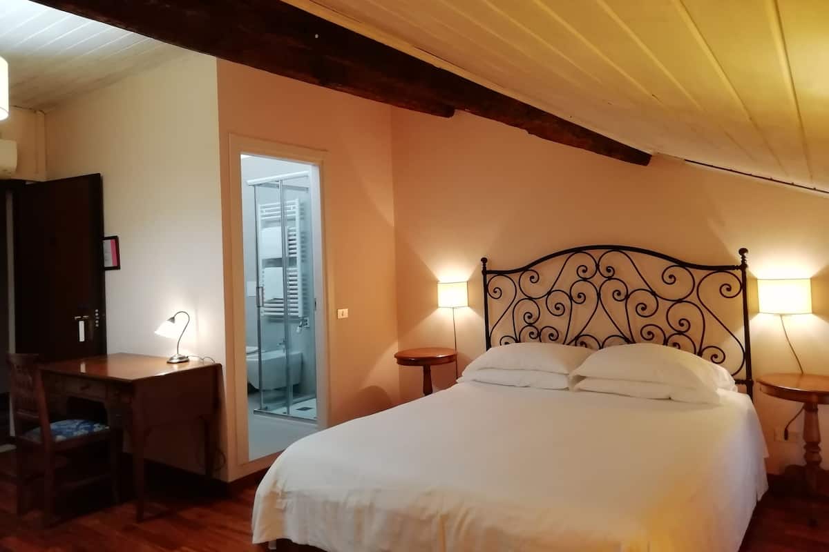 A bedroom with a bed, bedside lamps, a desk, and a wardrobe.