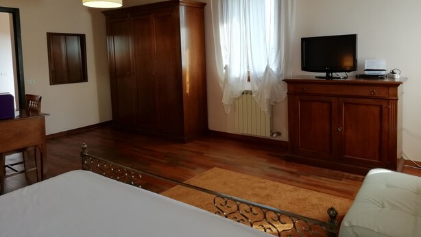 A room with a bed, wooden wardrobe, TV, and a radiator. - Locanda degli Ulivi (Arcugnano)