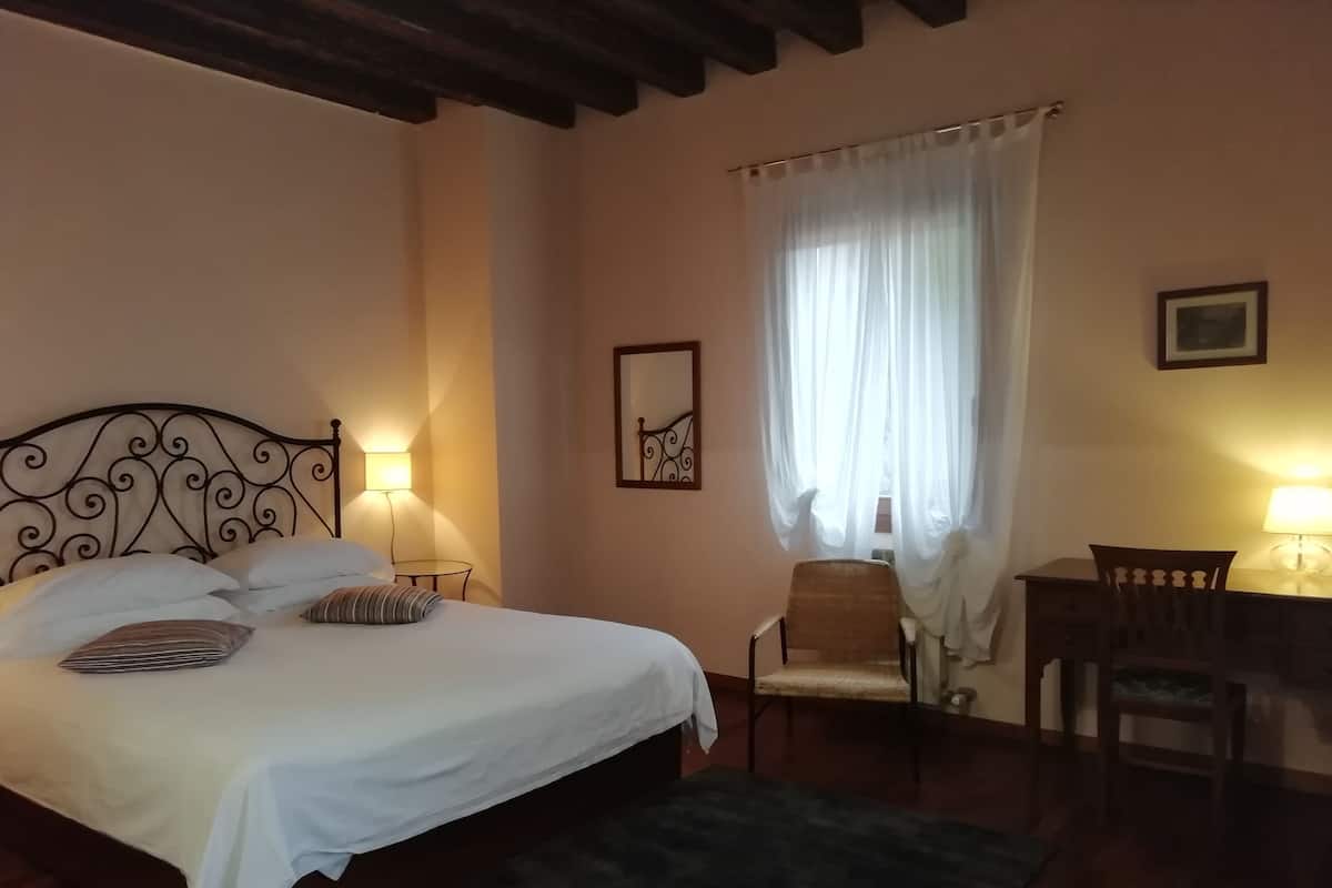A bedroom with a bed, bedside lamps, a chair, a desk, and a window with curtains.