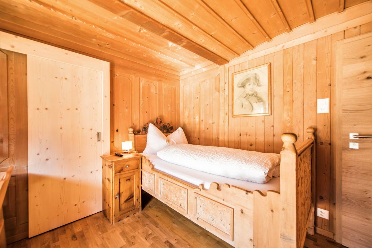 A wooden cabin bedroom with a bed, nightstand, and a painting on the wall.
