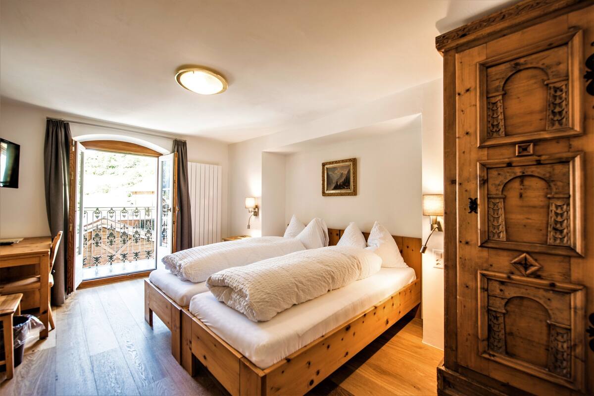 A double bed with white linens, a wooden desk, and a large wooden cabinet.