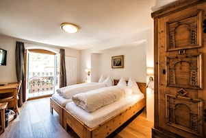 Uma cama de casal com roupa de cama branca, uma escrivaninha de madeira e um armário grande de madeira.