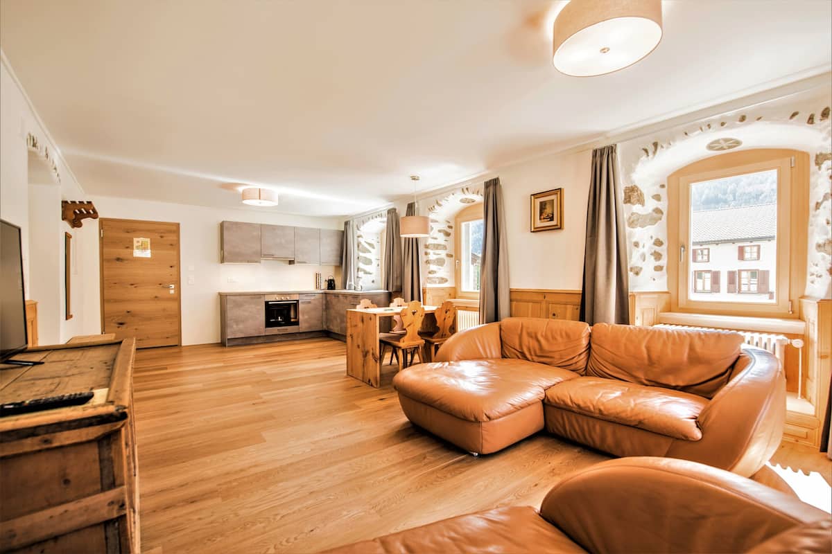 A modern living room with a wooden floor, a leather sofa, a dining area, and a kitchen.