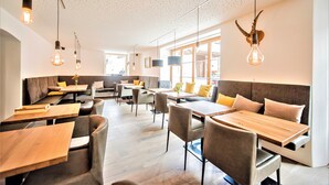 Un restaurante moderno con mesas y sillas de madera, techo alto con vigas a la vista e iluminación colgante.