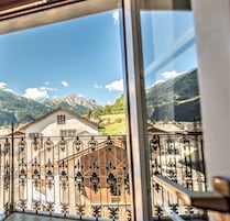 Varanda com grades de ferro forjado com vista para uma paisagem montanhosa e uma casa ao fundo.