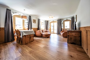 Um quarto espaçoso com piso de madeira, uma mesa de jantar com cadeiras, um sofá de couro e um armário de madeira.
