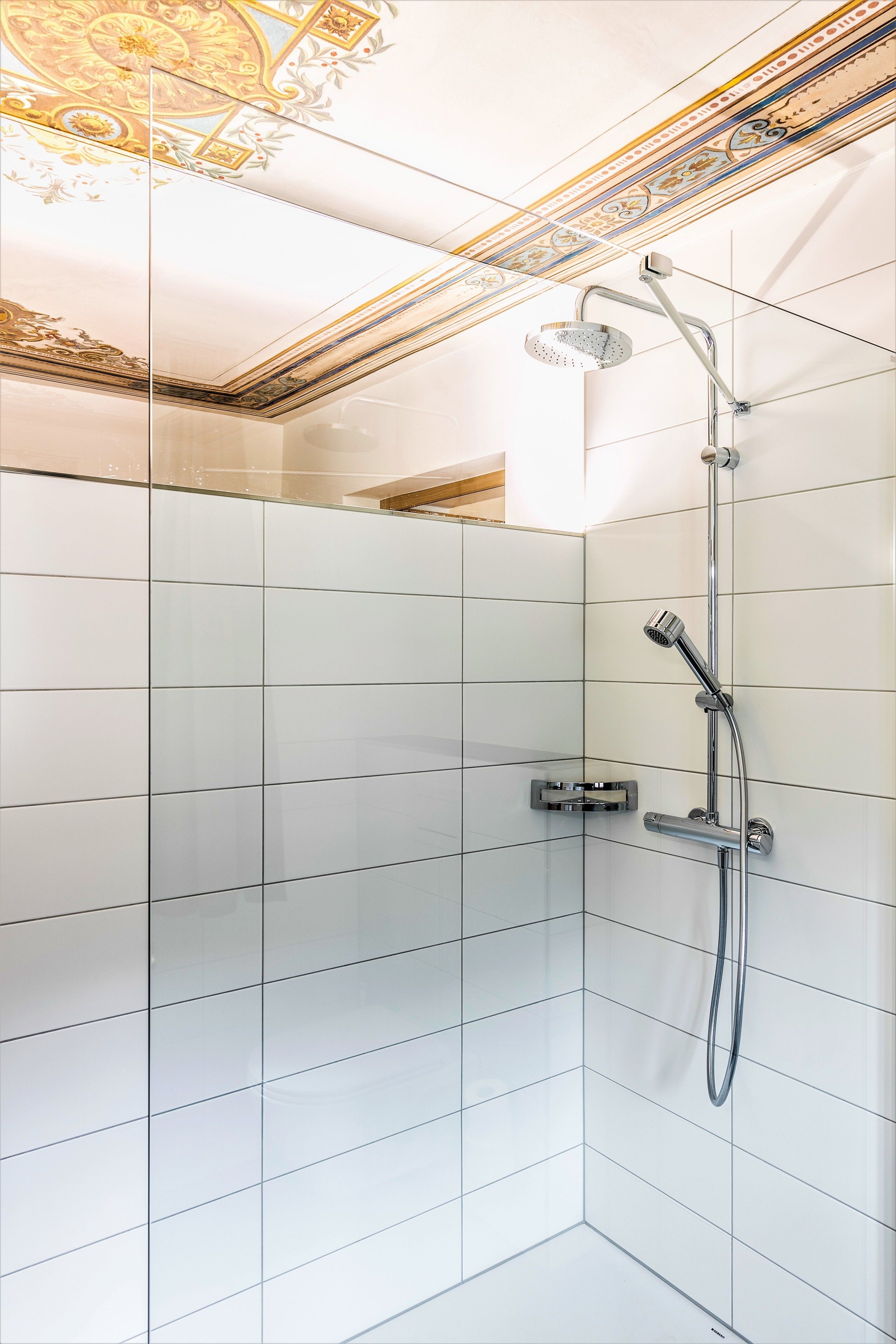 Una doccia moderna con soffione a mano e rubinetto a parete, con pareti rivestite di piastrelle bianche e un soffitto decorato.